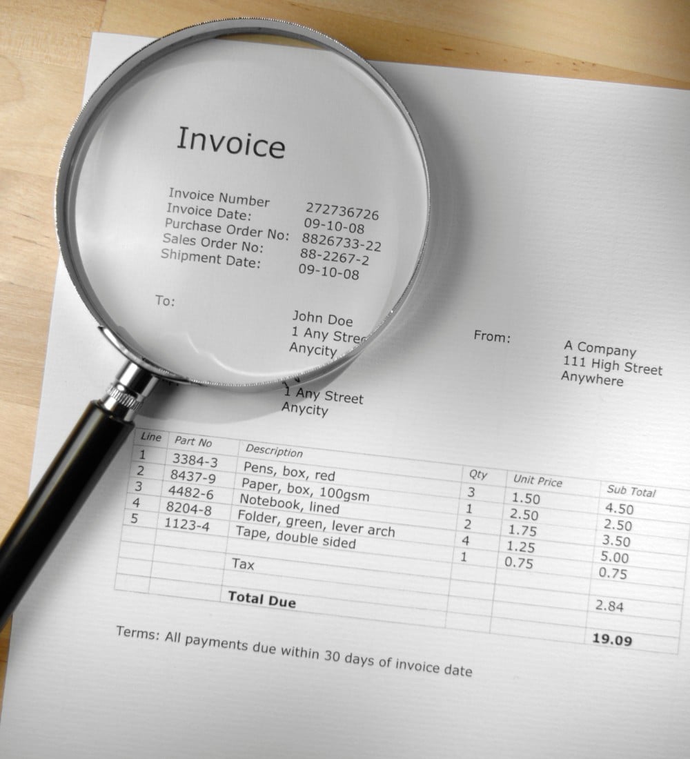 Pré-comptabilité Une facture posée sur un bureau, accompagnée d’une loupe pour en examiner les détails, illustrant le processus de vérification et de contrôle pré-comptable.