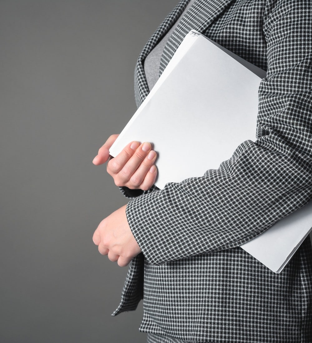 Assistante commerciale en rendez-vous Personne vêtue d’un tailleur à carreaux tenant un dossier blanc, illustrant le rôle d’une assistante commerciale prête pour une rencontre professionnelle.
